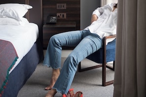 Ein Hotelzimmer mit einem Bett, einem Sessel, einem Nachttisch mit Telefon und Teppichboden.