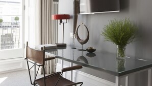 A modern living room with a glass coffee table, a red floor lamp, a wall-mounted TV, and a vase with green plants. - The Laslett Hotel (London)