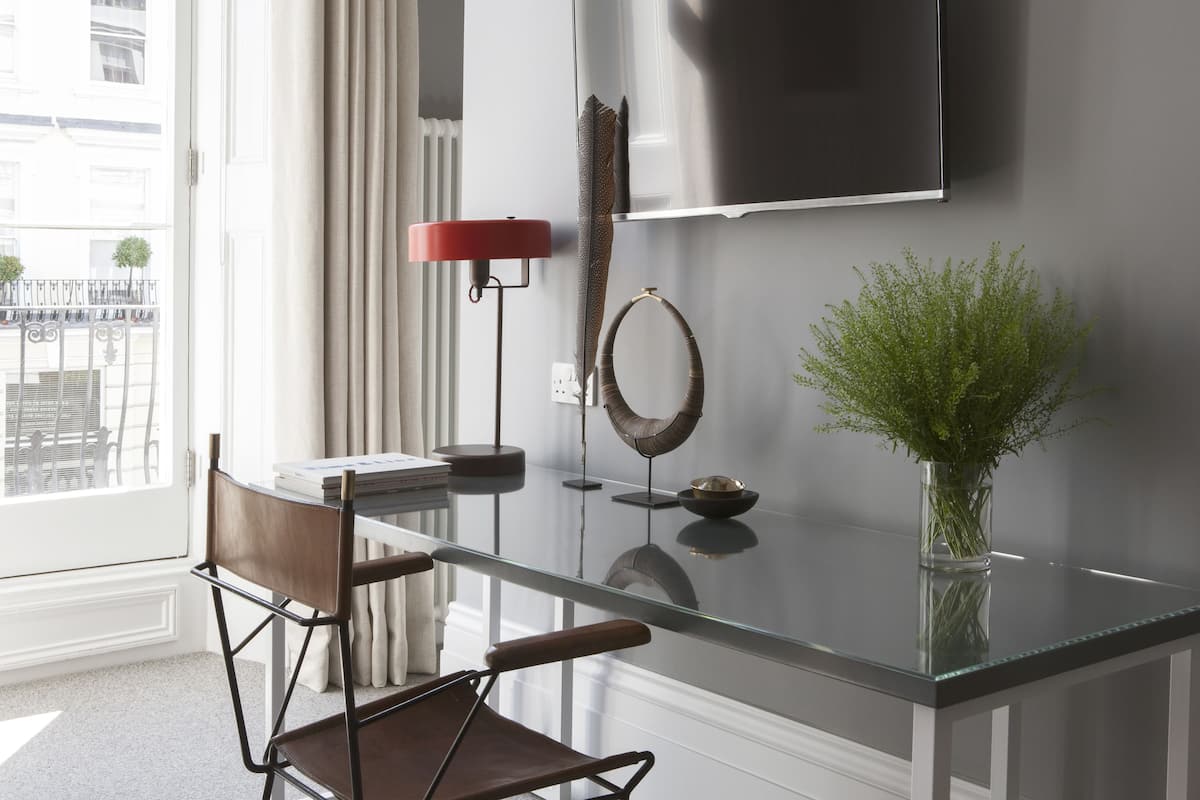 A modern living room with a glass coffee table, a red floor lamp, a wall-mounted TV, and a vase with green plants.