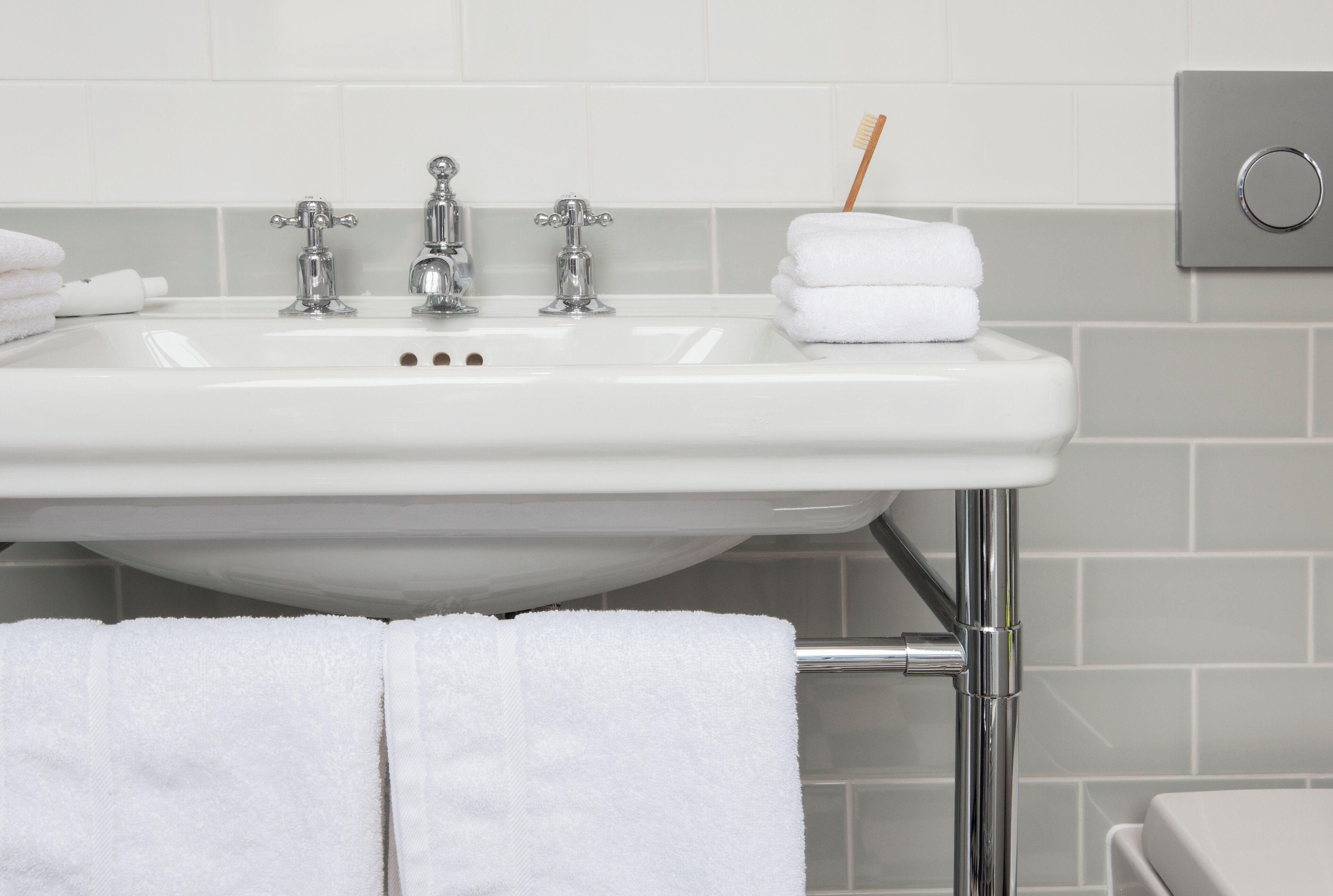 Un lavabo de salle de bain avec des robinets chromés, un porte-brosse à dents et des serviettes blanches soigneusement pliées.