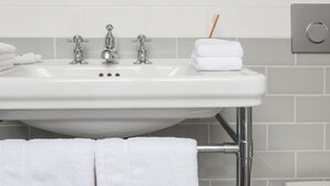 A bathroom sink with chrome fixtures, a toothbrush holder, and neatly folded white towels. - The Laslett Hotel (London)