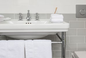Ein Badezimmerwaschbecken mit Chromarmaturen, ein Zahnbürstenhalter und ordentlich gefaltete weiße Handtücher.