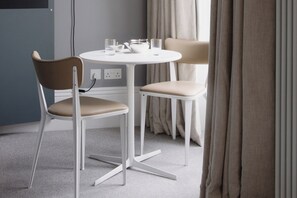 Ein modernes Zimmer mit einem runden Tisch, zwei Stühlen, einer Steckdose und einem fensterbepflanzten Fenster.