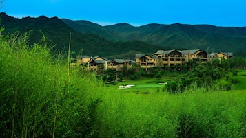 A resort with multiple-story buildings, a golf course, and lush green hills in the background.