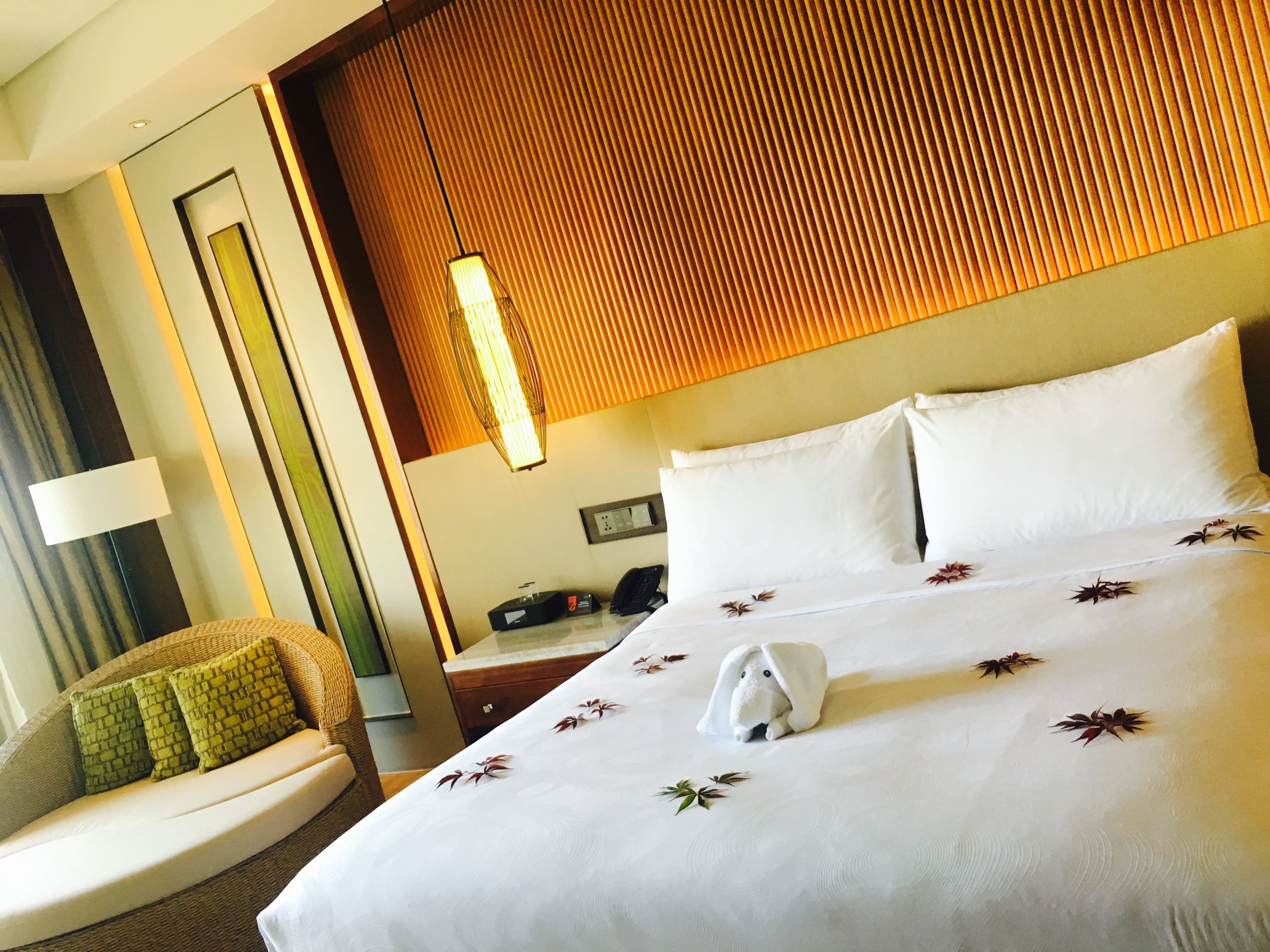 Habitación de hotel con una cama grande, una silla con cojines verdes, un cabecero de madera y una lámpara fijada a la pared.