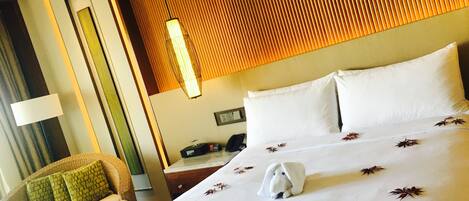 A hotel room with a large bed, a chair with green cushions, a wooden headboard, and a wall-mounted lamp.