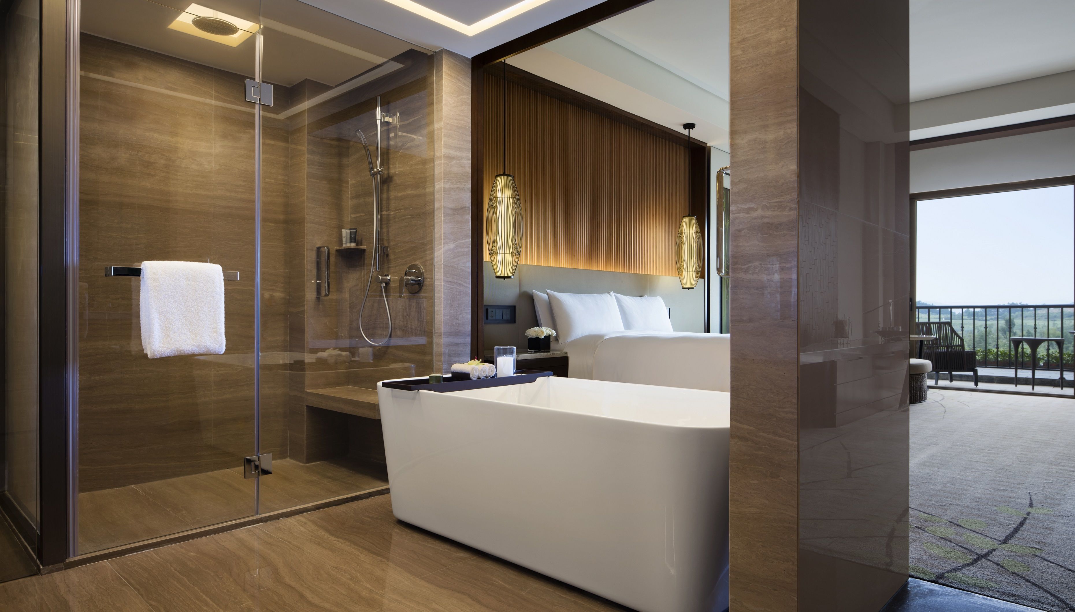 A modern bathroom with a glass-enclosed shower, a large bathtub, and a bed with a view of the outdoors.