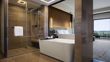 A modern bathroom with a glass-enclosed shower, a large bathtub, and a bed with a view of the outdoors.