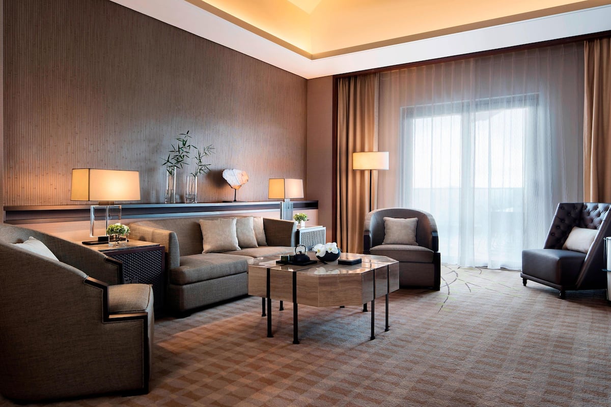 Une chambre d’hôtel moderne dotée d’une grande fenêtre, d’un canapé, d’un fauteuil, d’une table basse et d’une lampe.
