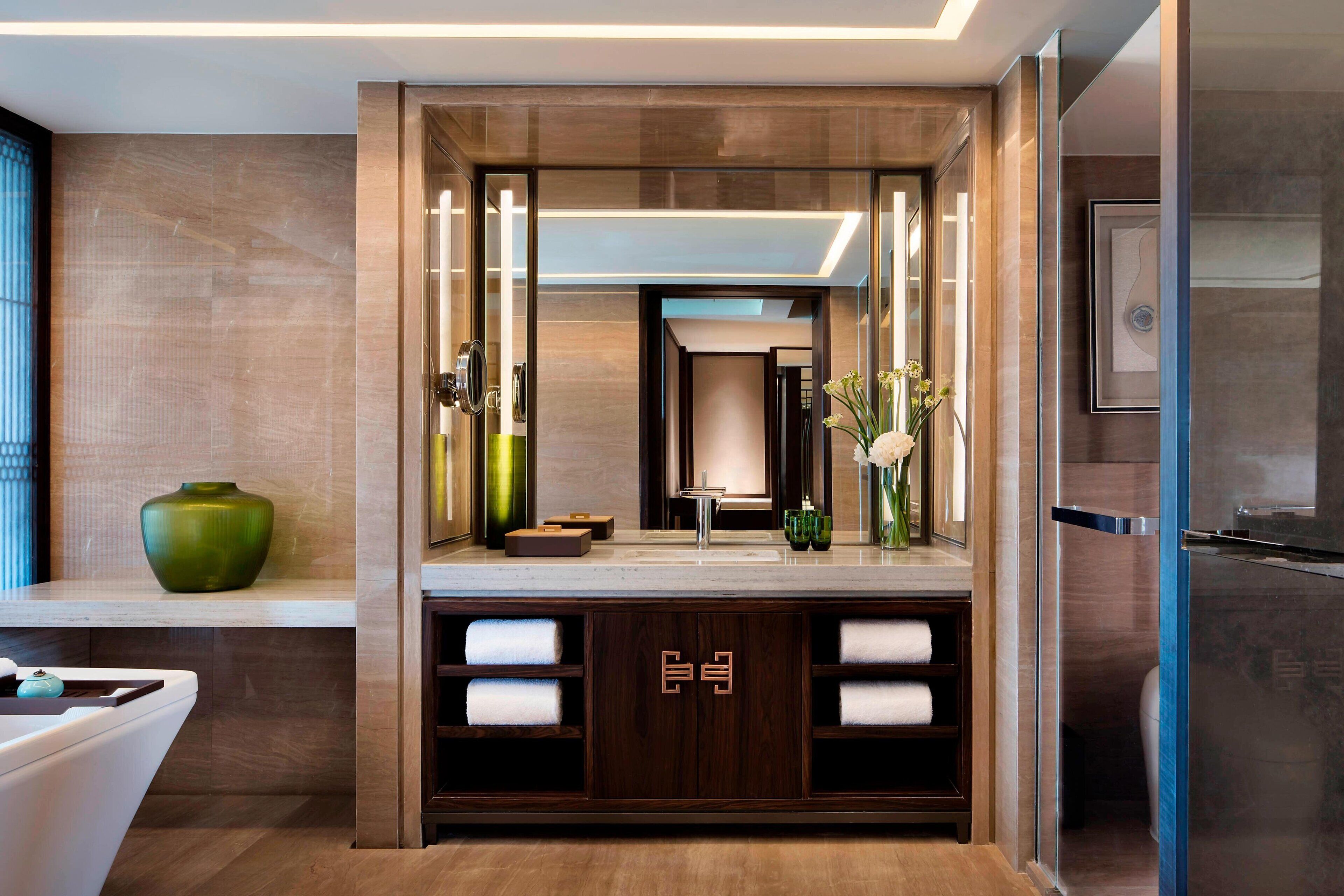 A modern bathroom with a large mirror, a sink, and a vanity with towels.