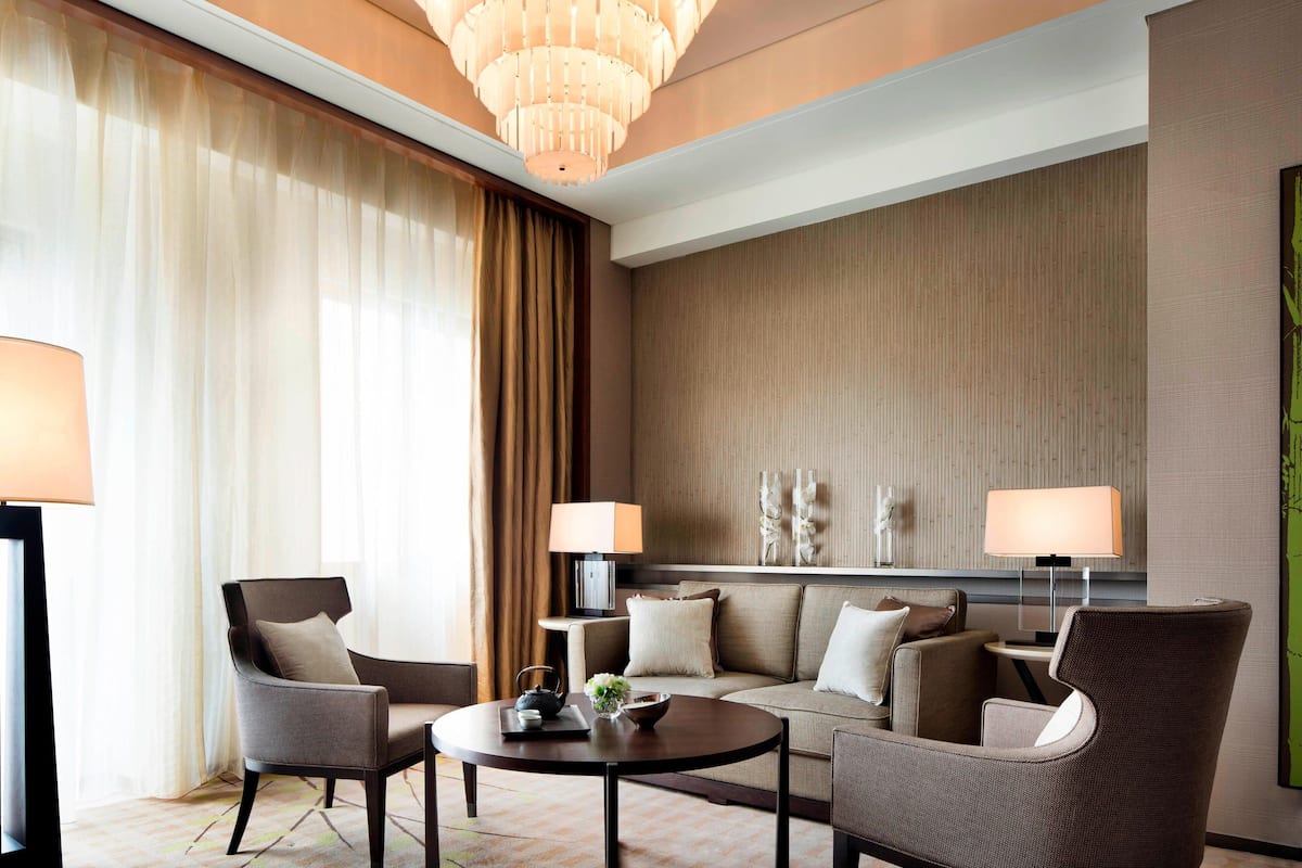 Une chambre d’hôtel moderne comprenant un canapé, deux fauteuils, une table basse et un lustre.