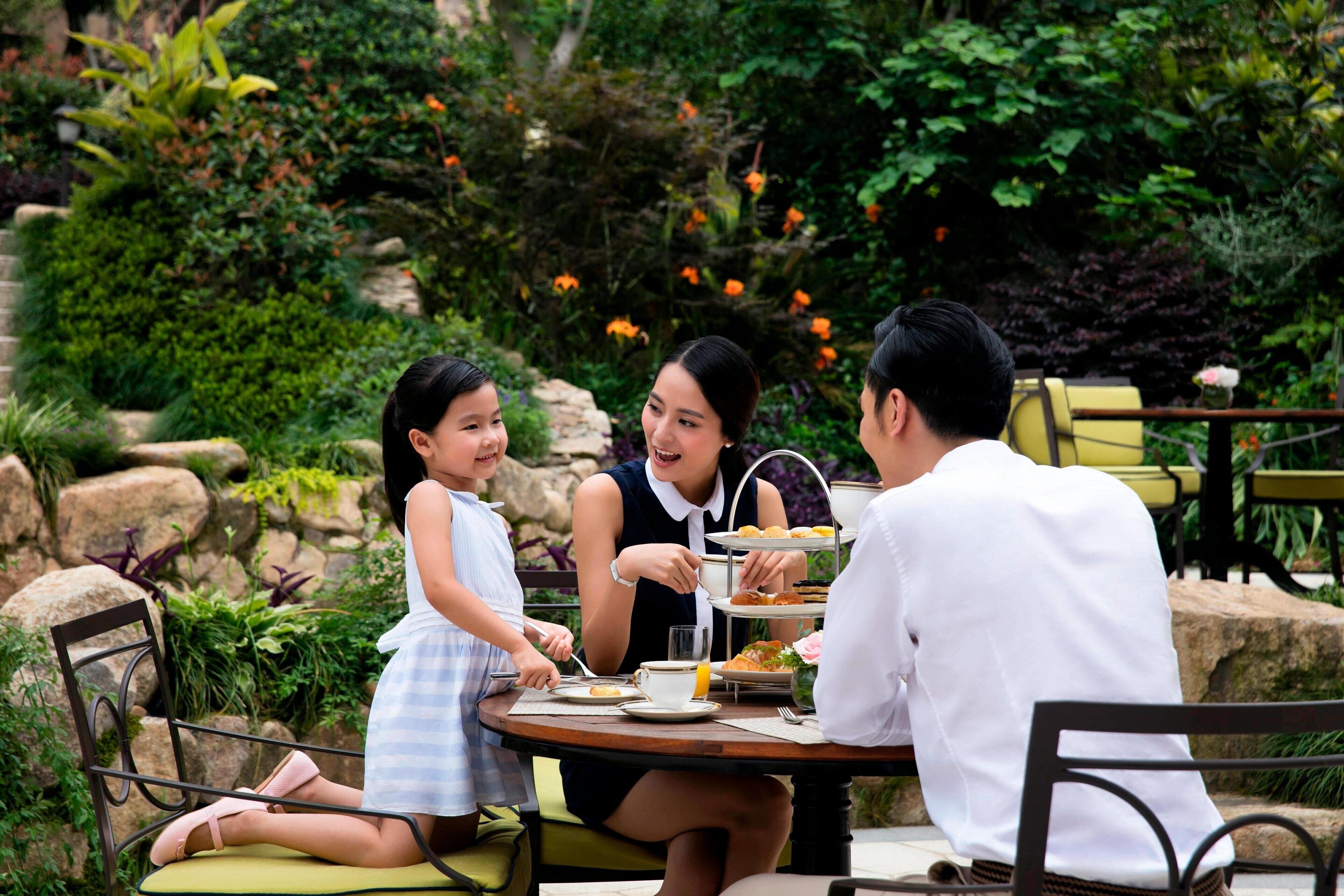 A group of people dining at an outdoor table with a garden view.