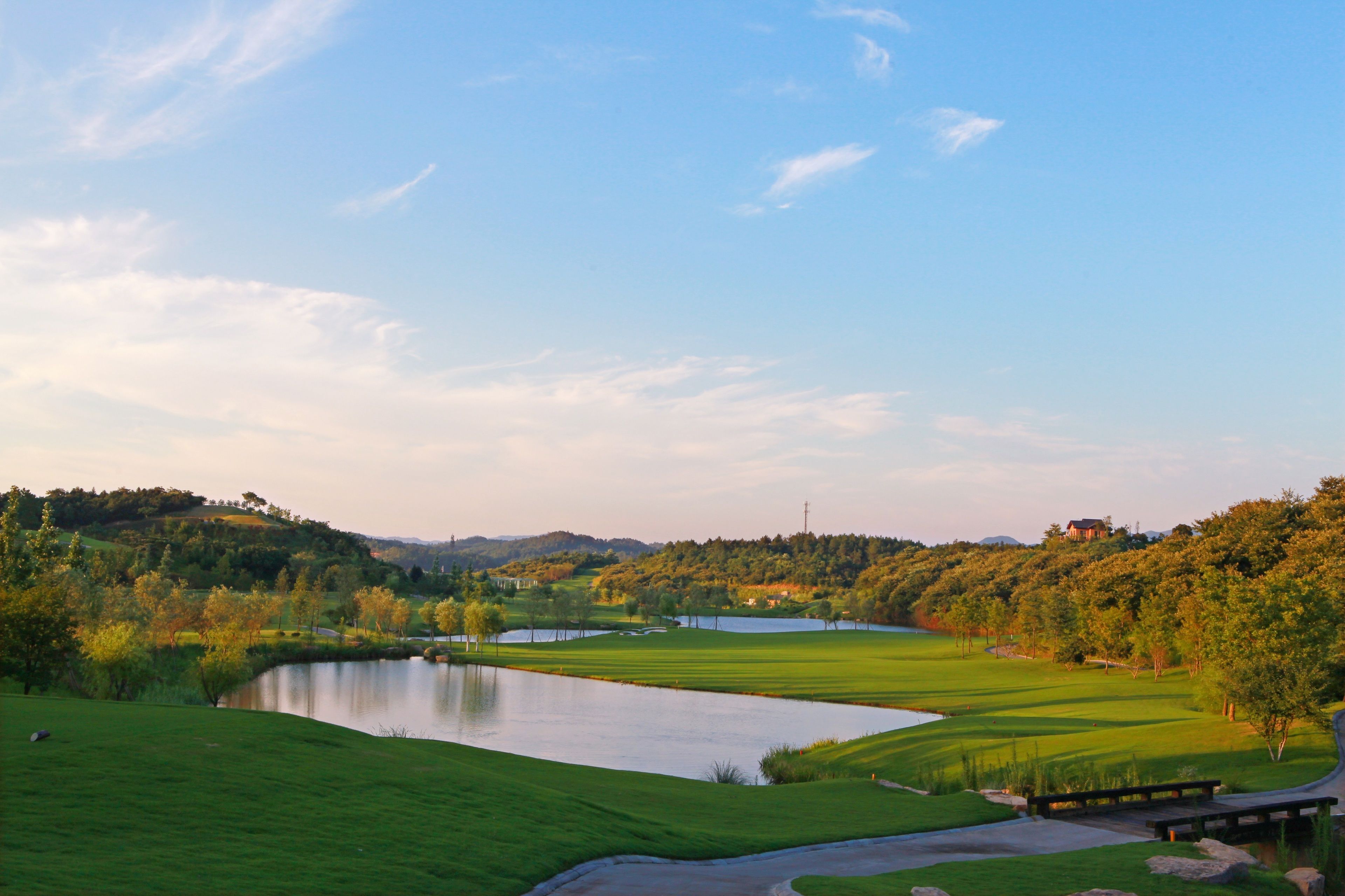 A golf course with a pond, green hills, and a clear sky.