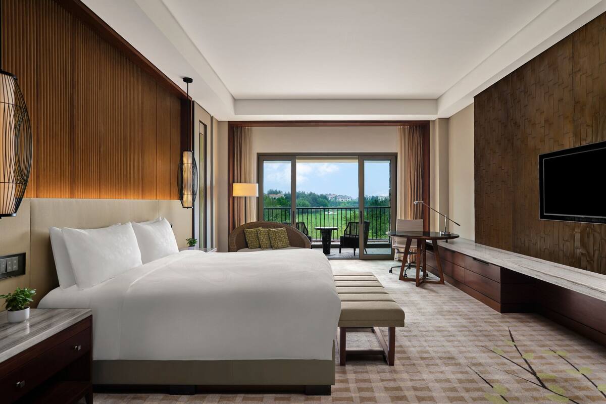 Une chambre d’hôtel avec un grand lit, un bureau, une chaise, une télévision et un balcon avec vue.