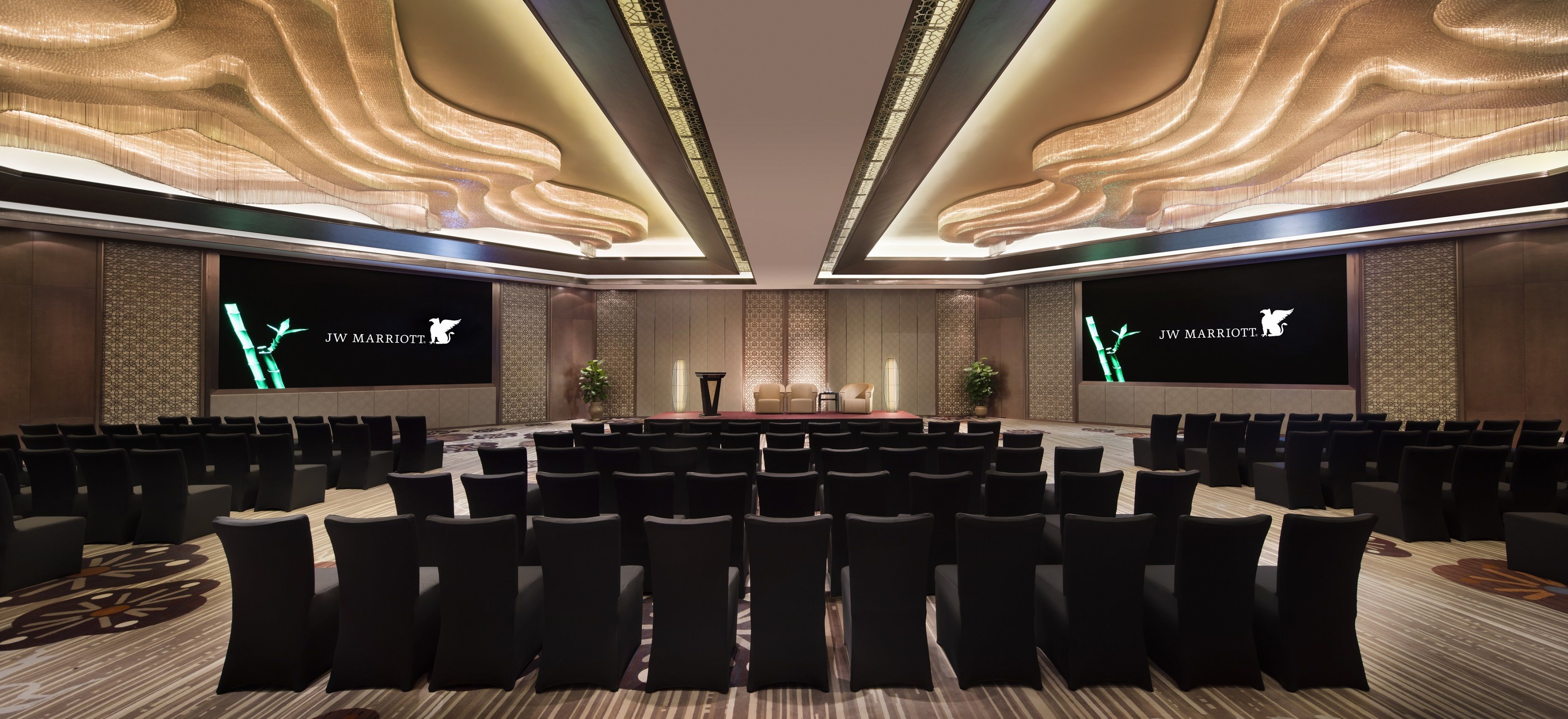 A conference room with rows of chairs, a stage, and screens displaying the JW Marriott logo.