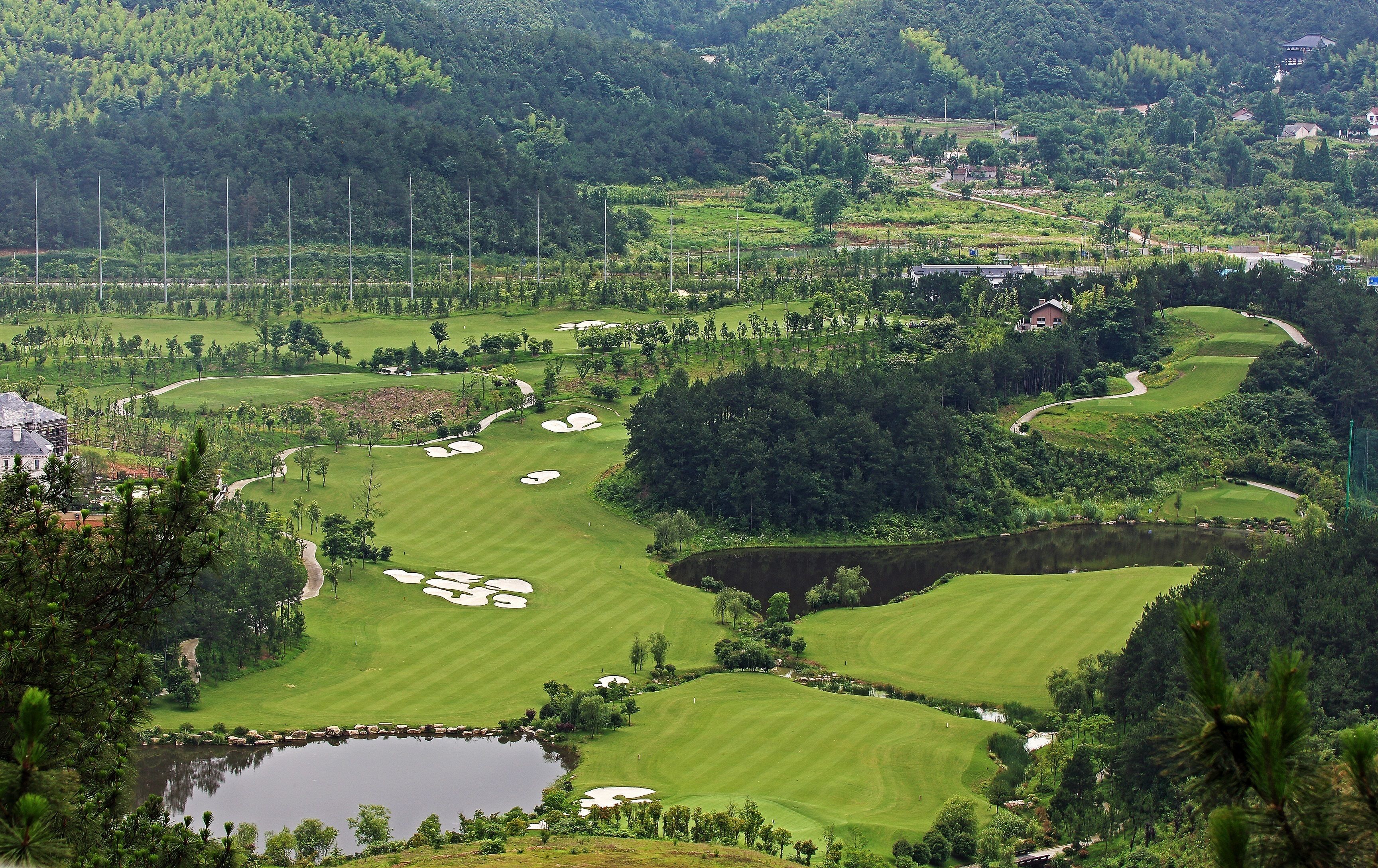 A golf course with multiple holes, water hazards, and surrounding forested hills.
