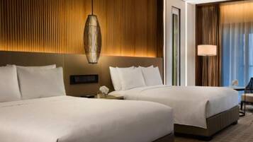 A hotel room with two beds, a wooden panel wall, a hanging light fixture, and a view of the outside through a window with curtains.