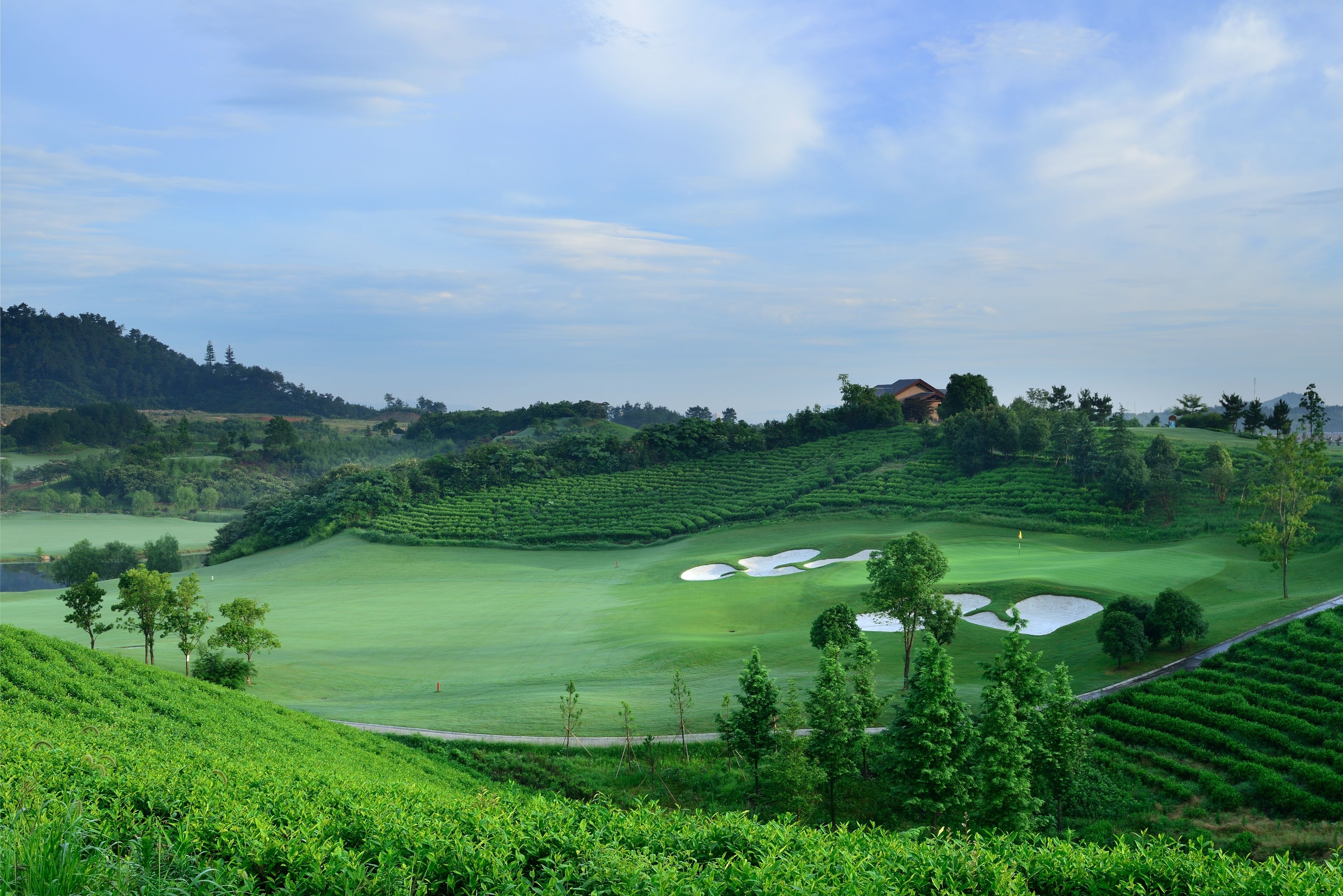 Un parcours de golf avec des collines douces, un étang et un petit bâtiment visible au loin.