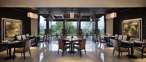 A spacious dining area with multiple tables and chairs, large windows offering a view of trees and mountains, and decorative wall art.