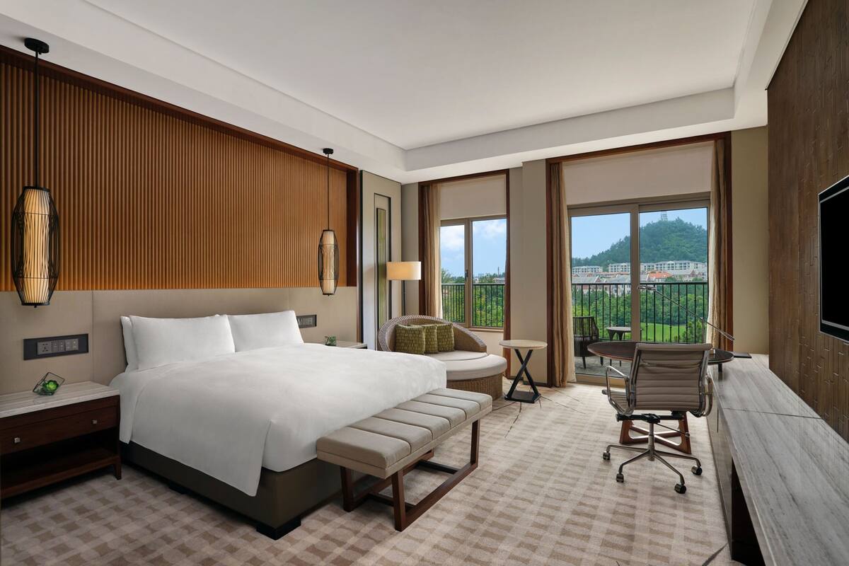 Une chambre d’hôtel avec un grand lit, un bureau, une chaise, une petite table et un téléviseur.