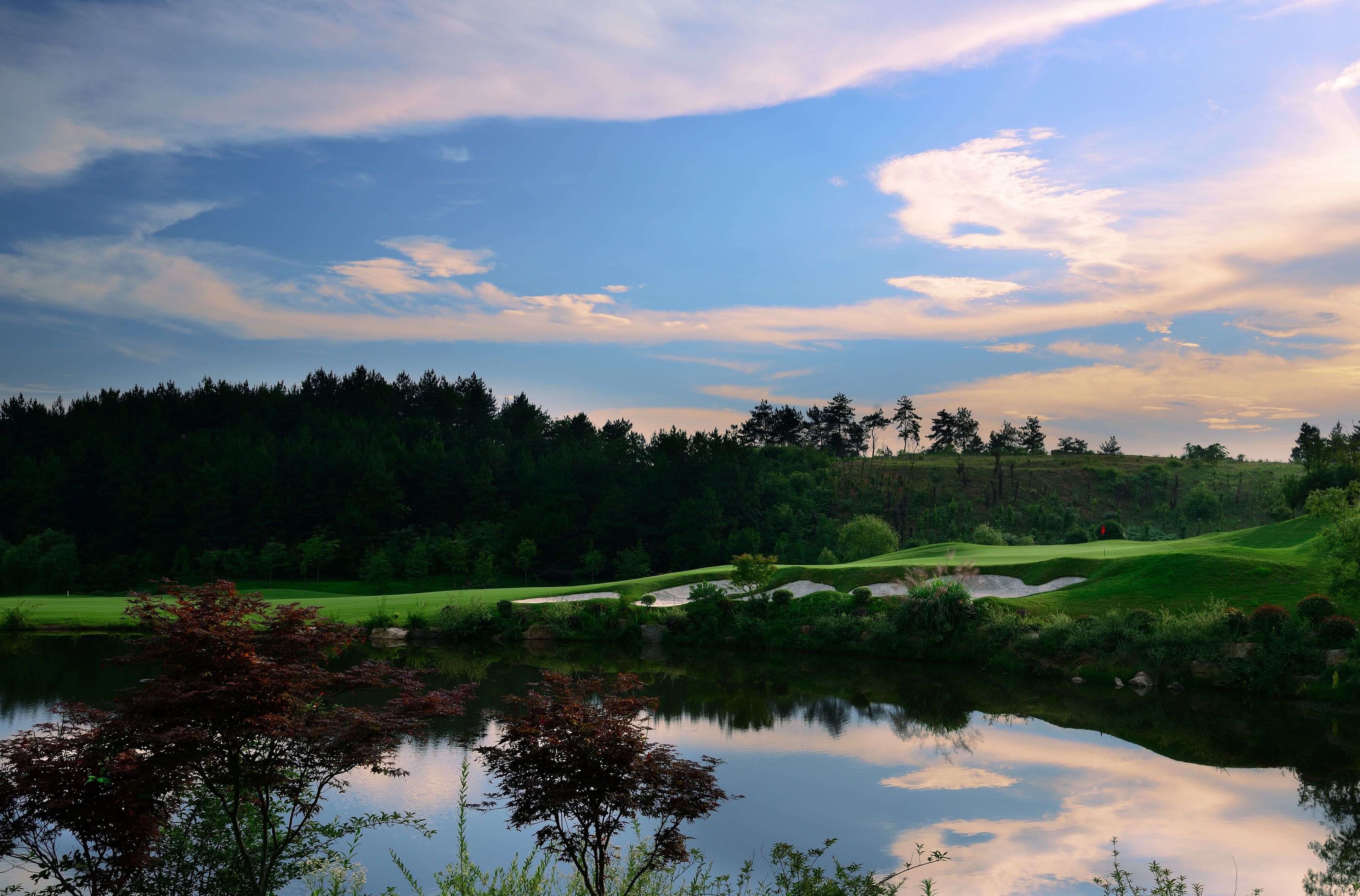 Rauhallinen maisema, jossa lammen pinnasta heijastuu taivas. Alueen ympärillä on vehreää kasvillisuutta ja sen läheisyydessä sijaitsee golfkenttä.