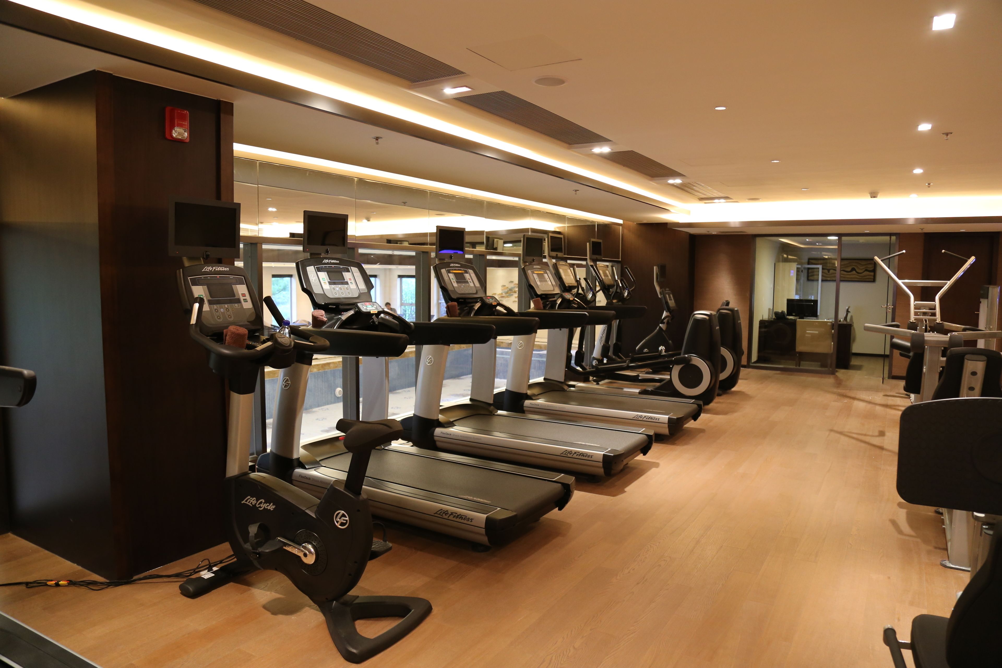 Un gimnasio con cintas de correr, bicicletas estáticas y un muro de espejos.
