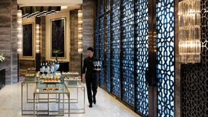 A hotel lobby with a modern chandelier, a waiter carrying trays, and a decorative wall with intricate patterns.