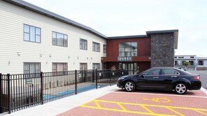 Een modern gebouw met een 'QUEST' bord, een zwarte auto die er voor geparkeerd staat en een parkeerplaats aangepast voor rolstoelen.