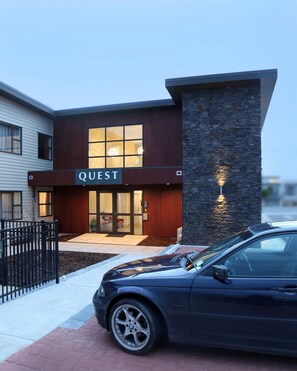 A modern building with a 'QUEST' sign, a stone facade, and a parked car in front. - Quest Taupo Serviced Apartments (Taupo)