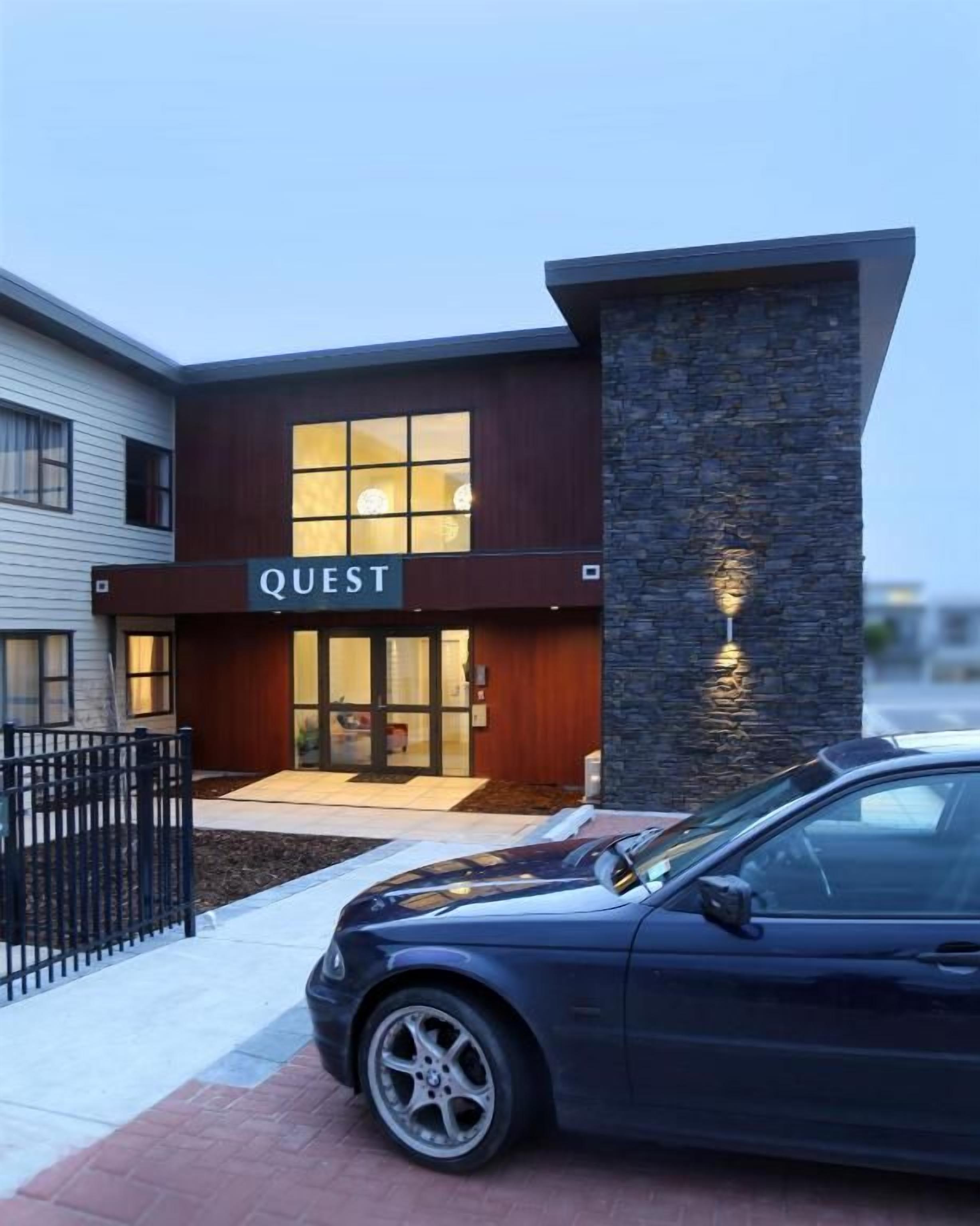 A modern building with a 'QUEST' sign, a stone facade, and a car parked in front.