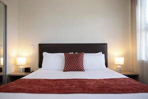 Une chambre d’hôtel avec un grand lit, deux lampes de chevet, un plaid rouge et un coussin à motifs.