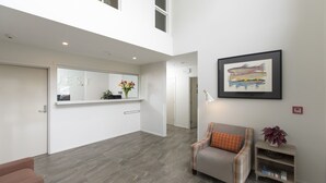 Un vaste espace de vie doté d’un haut plafond, une cuisine moderne avec des meubles blancs, une œuvre d’art encadrée au mur et un coin salon confortable avec un canapé et une table d’appoint.