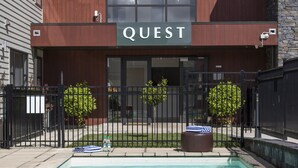 Un bâtiment moderne avec une piscine à l’avant, portant l’inscription « QUEST ».