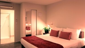 Une chambre d’hôtel avec un lit, une table de chevet avec une lampe, une plante en pot et un miroir.