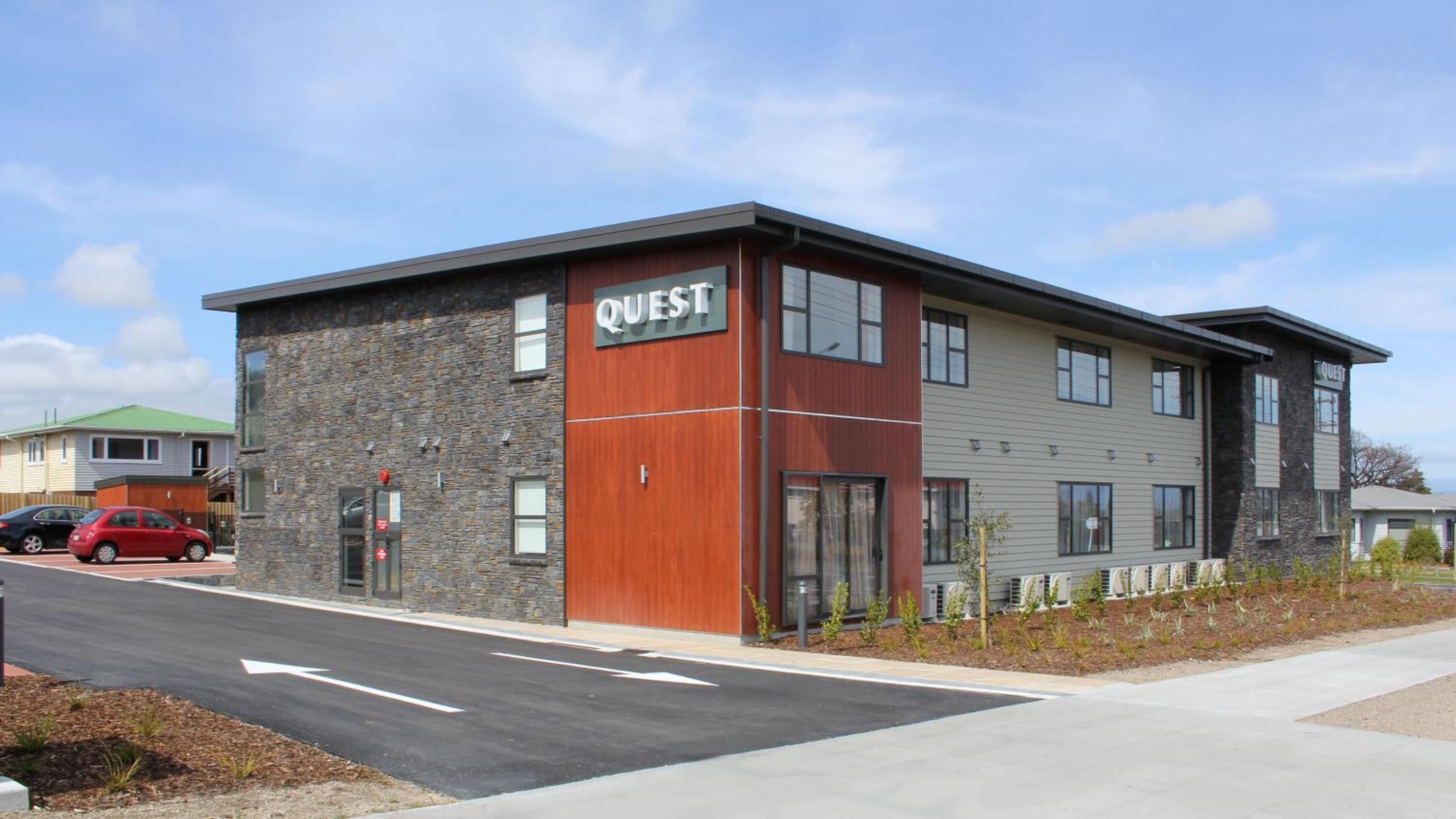 A modern building with a stone facade and a wooden section labeled "QUEST".