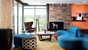 A modern living room with a stone fireplace, a blue armchair, a round coffee table, and a large window offering a view of the outdoors.