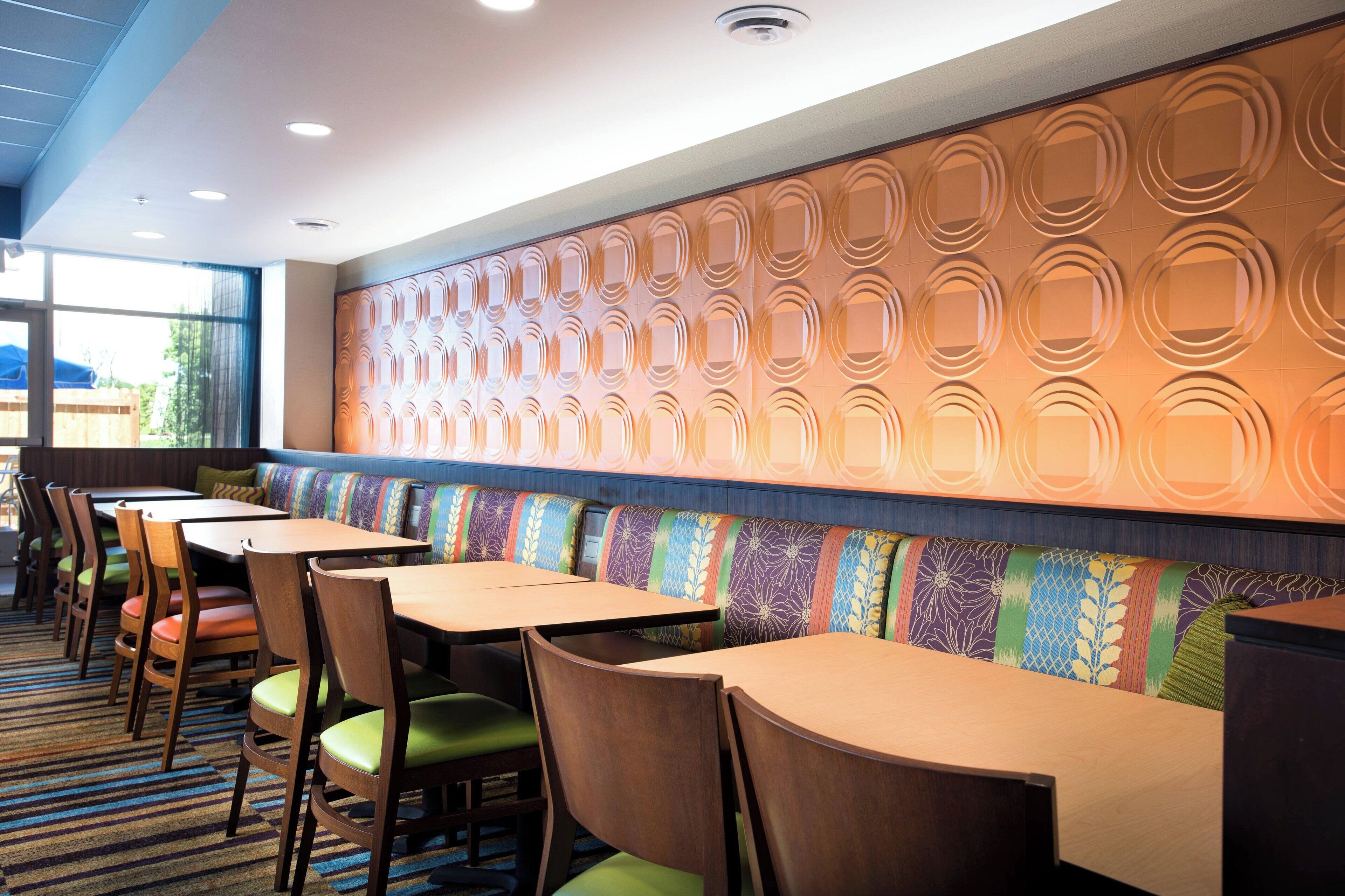 Un restaurante con cabinas y mesas, un muro con diseño y suelo alfombrado.