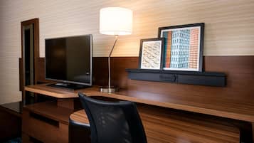 Et hotelværelse med skrivebord i træ, et fladskærms-tv, en lampe og to indrammede kunstværker.