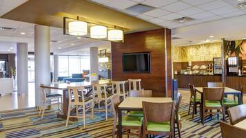 A hotel lobby with a large seating area, a television mounted on the wall, and a coffee station.