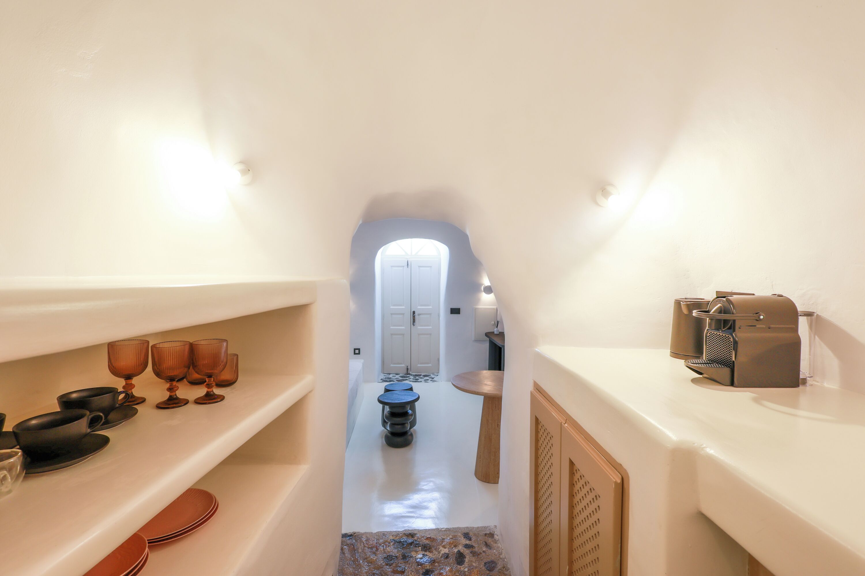 A narrow hallway with white walls, a small table with a cup and saucer, and shelves with glasses and plates.