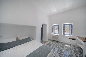 A bedroom with a bed, a small desk, and two windows. - Luna Santorini Suites (Santorini)