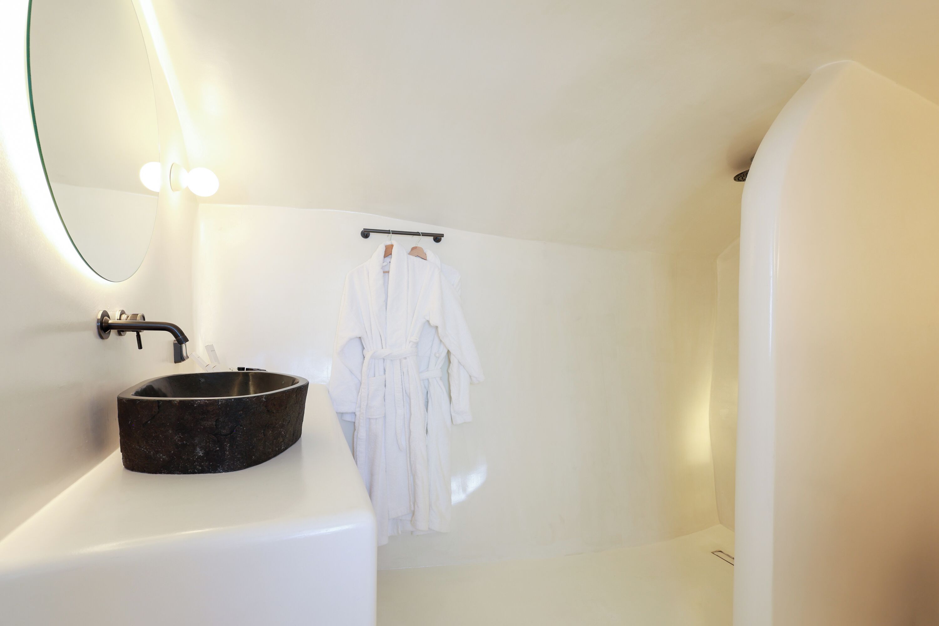 A modern bathroom with a round sink, a mirror, and a white robe hanging on a rack.