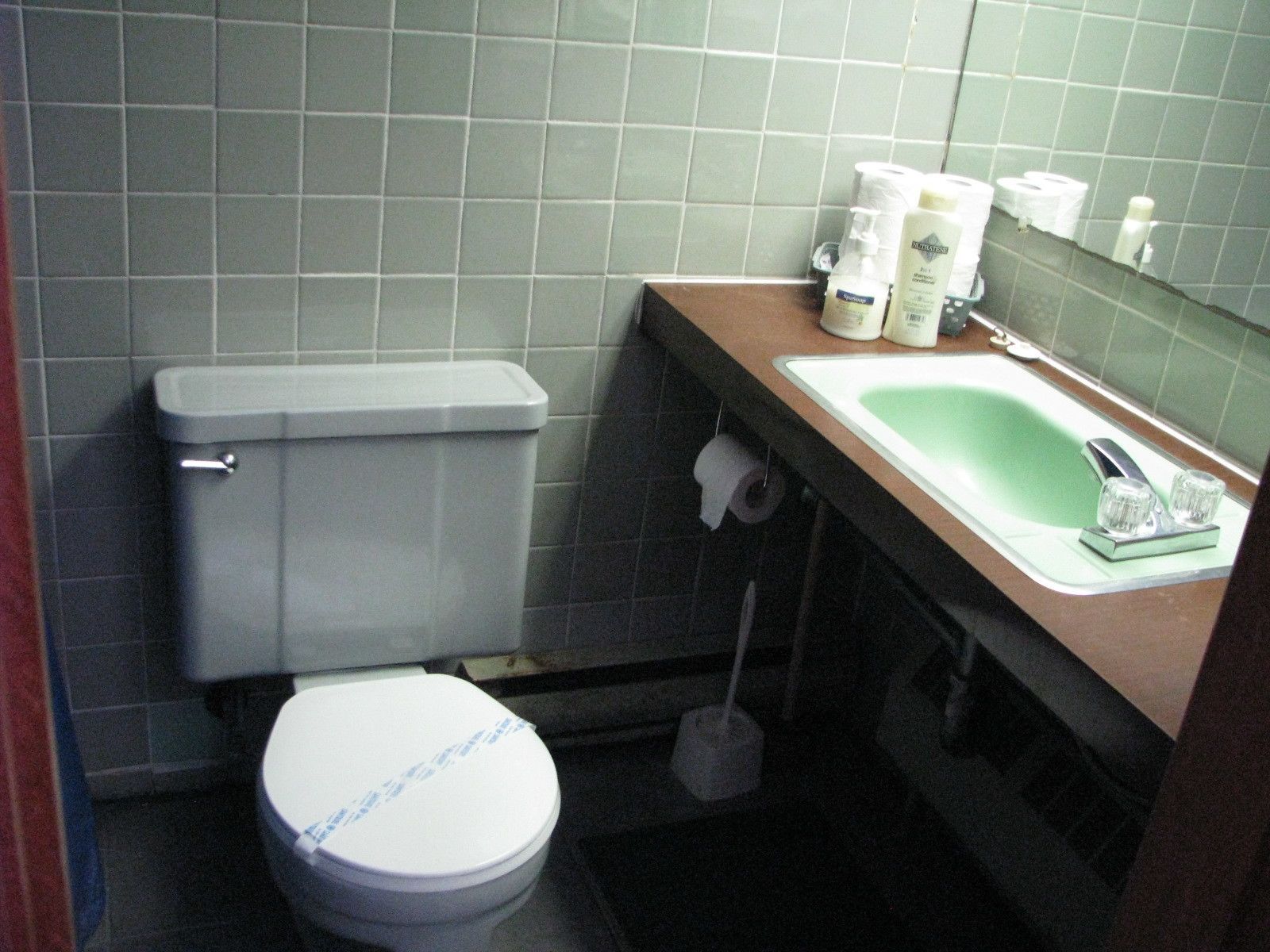 A small bathroom with a toilet, sink, and mirror. There are toiletries on the sink counter.