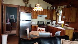 A cozy living room with a black leather sofa and a dining table, connected to a kitchen with wooden cabinets and modern appliances.