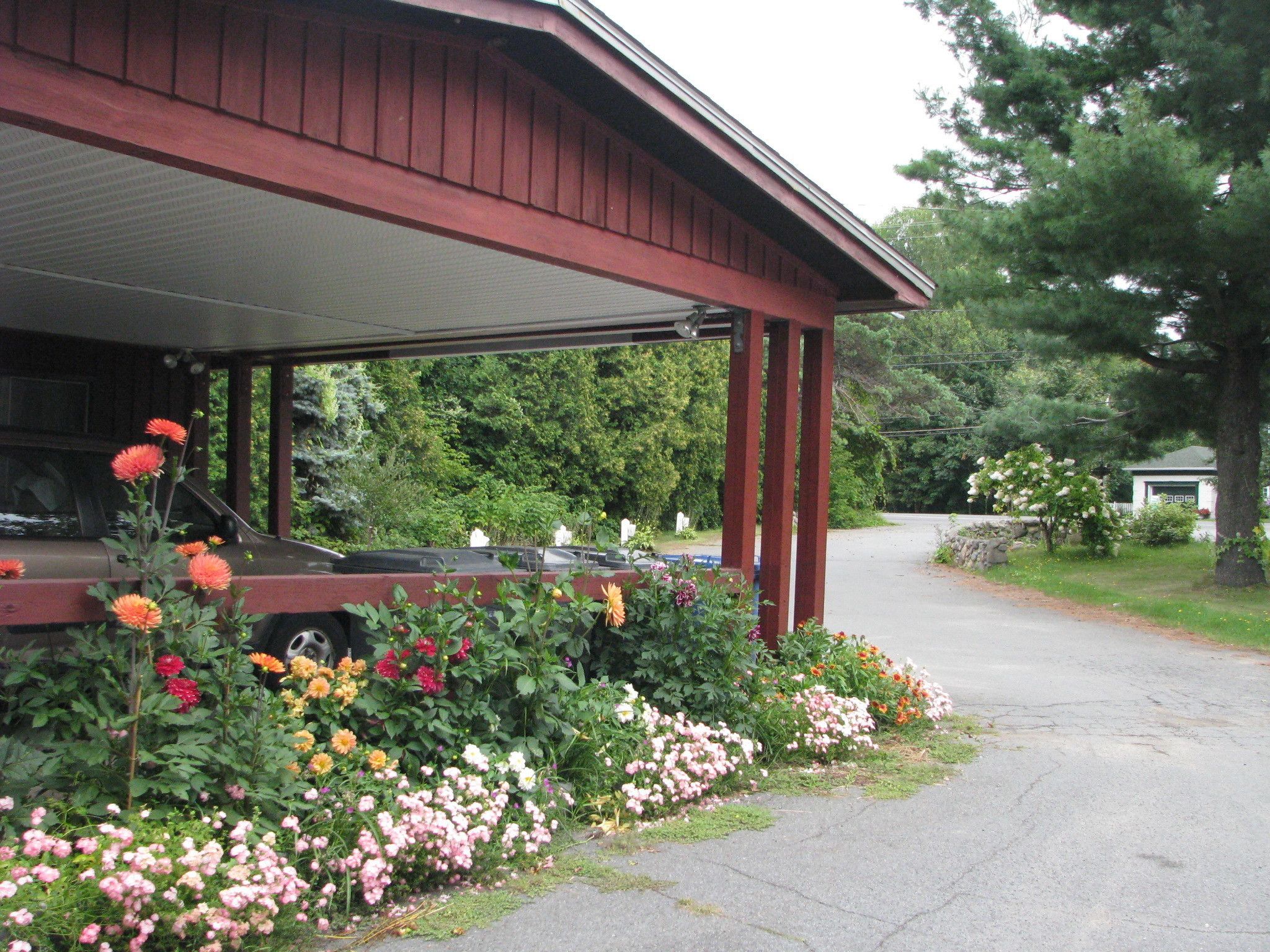 A covered porch with a car parked underneath, surrounded by a variety of colorful flowers.