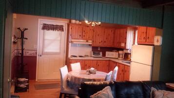 A compact living space with a dining area, a kitchen with wooden cabinets, a black leather couch, and a coat rack.