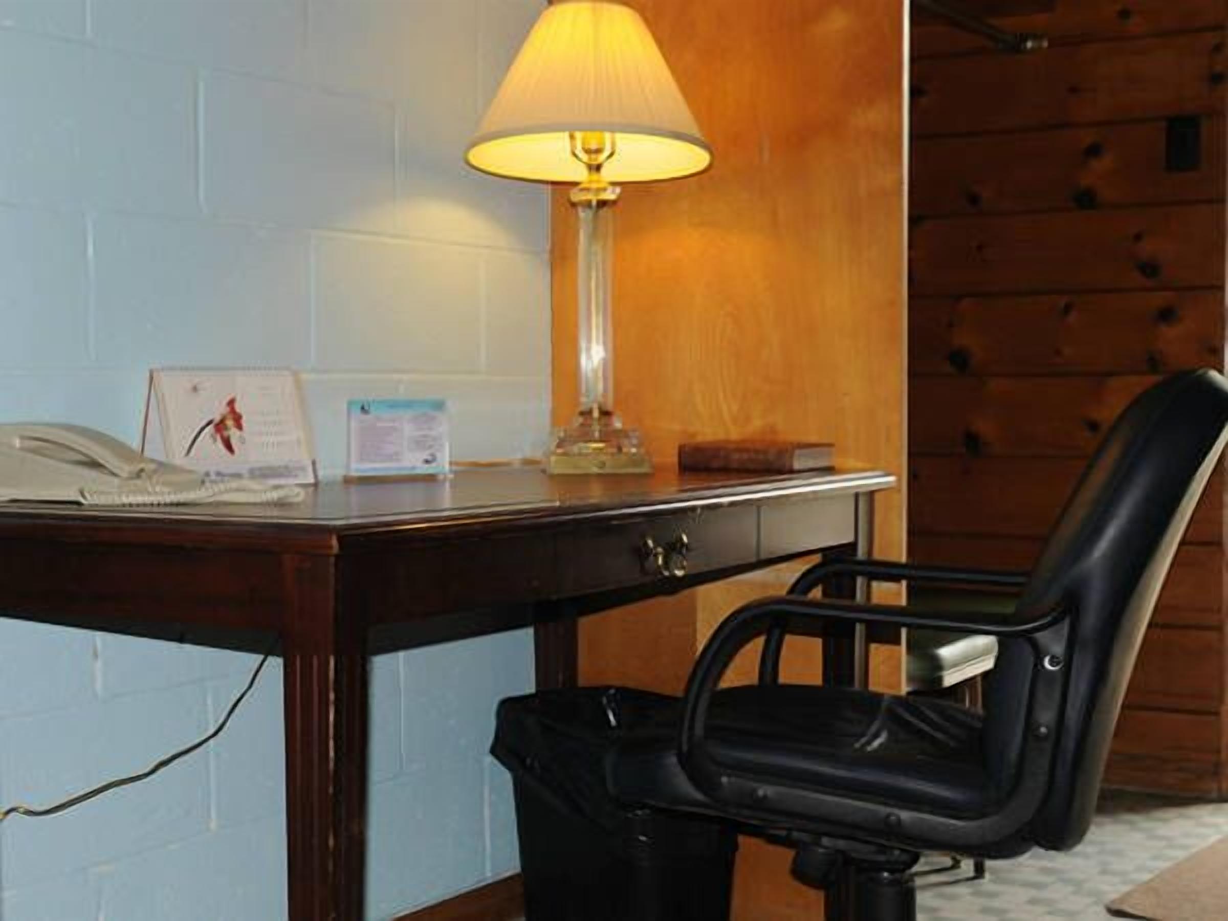 A wooden desk with a lamp, a telephone, and a chair.