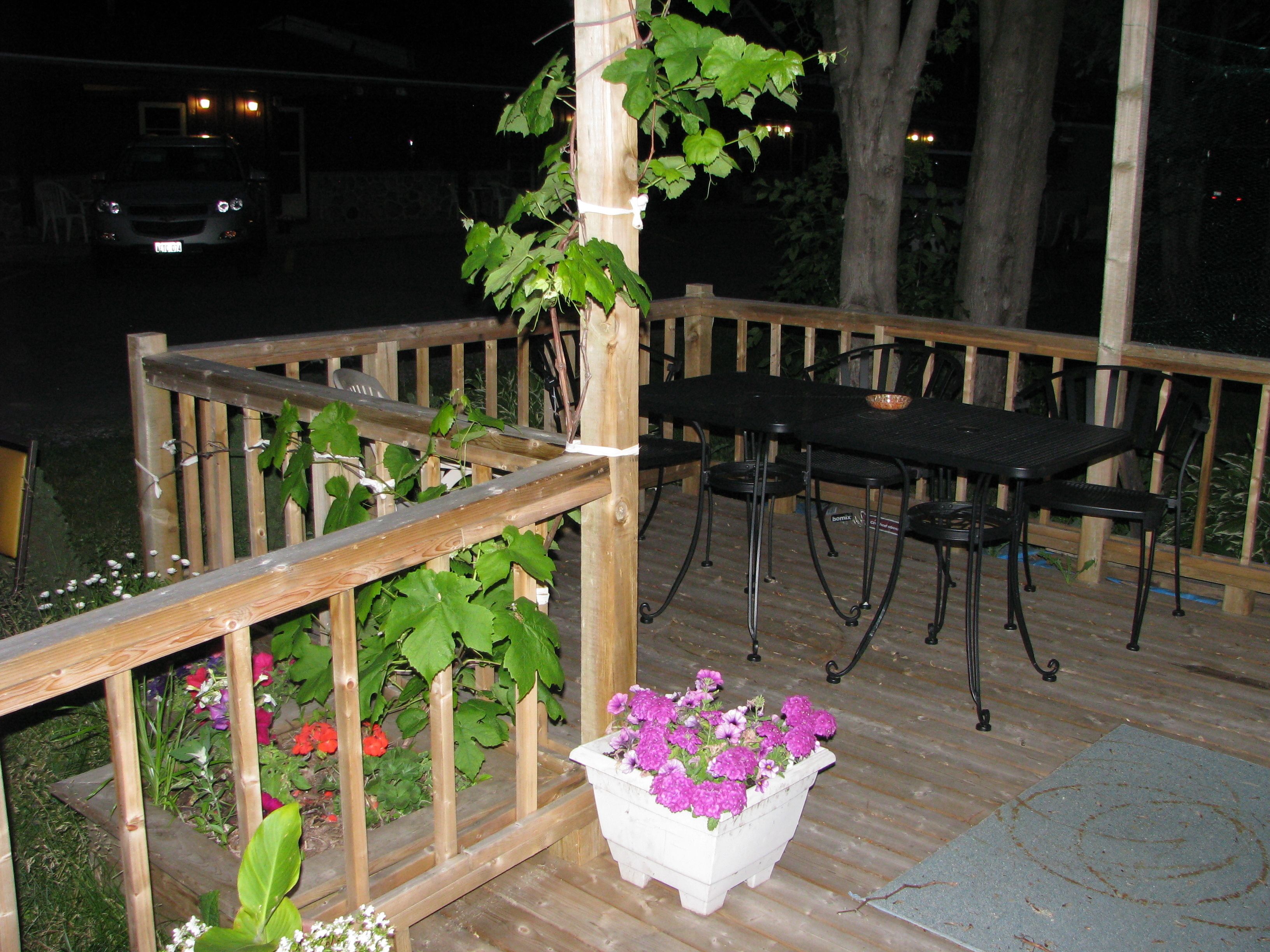 A wooden deck with a table and chairs, surrounded by a wooden railing and potted plants.
