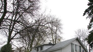 A two-story house with a porch, surrounded by trees and a grassy yard.