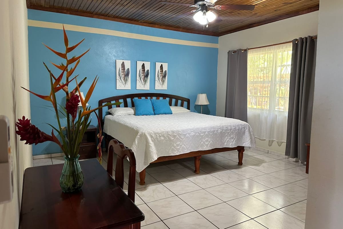 A bedroom with a bed, a nightstand, a table with a vase, and a ceiling fan.